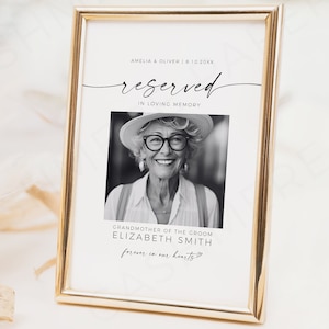 Pode incluir: Uma fotografia emoldurada em ouro com fundo branco. A fotografia diz "reservado" em escrita cursiva e "em memória carinhosa". Uma fotografia em preto e branco de uma mulher usando óculos e um chapéu está no centro da fotografia. O texto abaixo da fotografia diz "Avó do noivo Elizabeth Smith para sempre em nossos corações".
