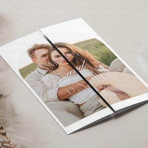 May include: A folded wedding invitation with a photo of a couple embracing in a field. The invitation features the names "Samantha and Daniel" in a white script font.