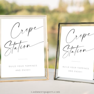 May include: Two gold and silver framed signs with white backgrounds and black text that reads "Crepe Station" and "Build your toppings and enjoy!"