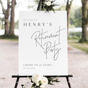 Puede incluir: Un letrero blanco sobre un caballete negro con el texto "WELCOME TO HENRY'S Retirement Party" en escritura negra. El letrero tambi&eacute;n dice "CHEERS TO 40 YEARS!" y una fecha. Flores blancas y vegetaci&oacute;n decoran la parte superior e inferior.