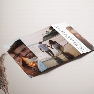 May include: A folded wedding invitation with a photo of a couple on the beach. The invitation is white with black text that reads "The Wedding Day". The date of the wedding is written in cursive on the front of the invitation.