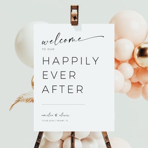 May include: White welcome sign with black text that reads "Welcome to our Happily Ever After Amelia & Oliver 10.08.20XX | Miami, FL". The sign is on a wooden easel with a cluster of peach and gold balloons behind it.