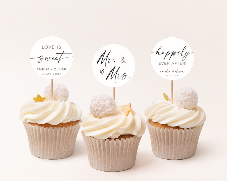 Pode incluir: Tr&ecirc;s cupcakes brancos com cobertura branca e granulado dourado. Cada cupcake tem um topo redondo de papel branco com texto preto. Os topos dizem "Love is sweet Amelia + Oliver 08.20.20XX", "Mr. & Mrs." e "Happily Ever After! Amelia + Oliver 08.20.20XX".