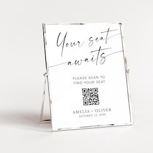 以下が含まれることがあります： 「Your seat awaits」と筆記体で書かれた銀色のフレームのサイン。 「Please scan to find your seat」という指示とQRコードが含まれています。 サインはアメリアとオリバーのもので、20XX年10月12日と日付が記されています。