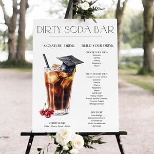 May include: A white sign with the text "DIRTY SODA BAR" and a detailed illustration of a Cherry Bomb drink. The sign lists soda and flavor options, including coconut, cherry, and raspberry. A graduation cap sits atop the drink.