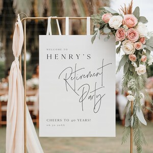 Puede incluir: Un letrero blanco con el texto "WELCOME TO HENRY'S Retirement Party" en escritura negra. El letrero est&aacute; decorado con un arreglo floral de rosas rosas y blancas y vegetaci&oacute;n. El letrero dice "CHEERS TO 40 YEARS!" y la fecha.