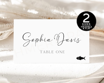 May include: White place card with black text. The name "Sophia Davis" is written in cursive script. Below the name is the text "Table One". A small black fish icon is in the bottom right corner.