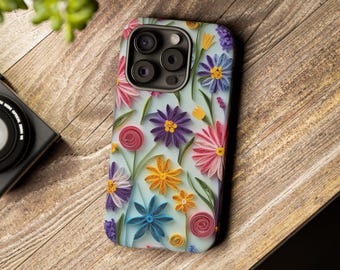 Puede incluir: Funda de teléfono con diseño floral. La funda tiene un fondo azul claro con flores de papel de colores. Las flores incluyen flores rosas, moradas, amarillas y azules con tallos verdes. La funda está sobre una superficie de madera.
