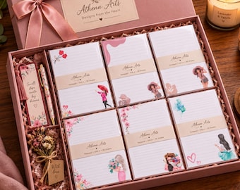 Könnte beinhalten: Eine rosa Geschenkbox mit sechs linierten Notizblöcken mit verschiedenen Illustrationen, einem Blumen-Lesezeichen mit dem Text Small steps create big dreams, einem passenden Stift und einem kleinen Trockenblumenstrauß mit einem With love-Anhänger.