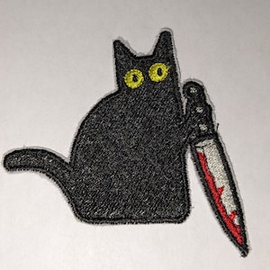 May include: Black embroidered patch of a cat holding a bloody knife. The cat has yellow eyes.