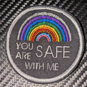 May include: A black and white embroidered patch with a rainbow and the text "You are safe with me".
