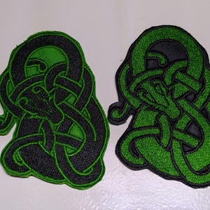 May include: Four embroidered patches with a green and black Celtic knot design. The knots are in the shape of a serpent or dragon.