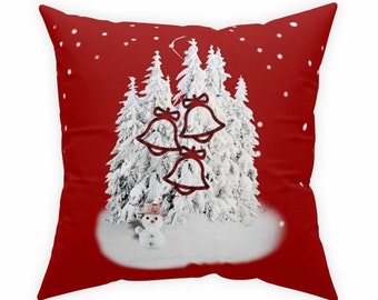 Op de afbeelding: Rood kussen met een besneeuwde bos scène en drie rode bellen die aan de takken hangen. Een sneeuwpop staat in de sneeuw onder de bomen.