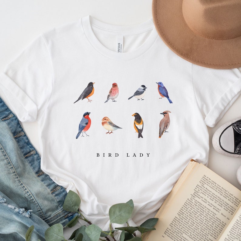 May include: White t-shirt with a graphic of various colorful birds and the text "Bird Lady".