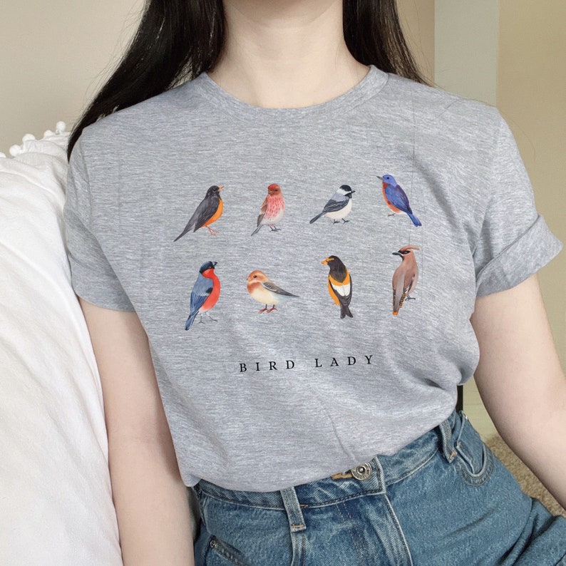 May include: Gray t-shirt with a graphic of nine different birds, including a blue jay, a cardinal, and a chickadee. The text "Bird Lady" is printed below the birds.