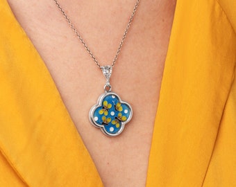 May include: A silver chain necklace with a blue and white enamel pendant featuring yellow flowers. The pendant is shaped like a four-leaf clover.