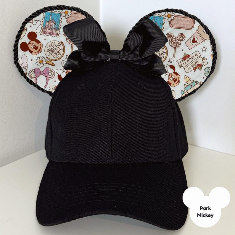 Puede incluir: Gorra de b&eacute;isbol negra con orejas de Mickey Mouse. Las orejas est&aacute;n decoradas con una tela estampada con Mickey Mouse, flores y el texto "I'd rather be at Disney". Un lazo negro se encuentra entre las orejas.