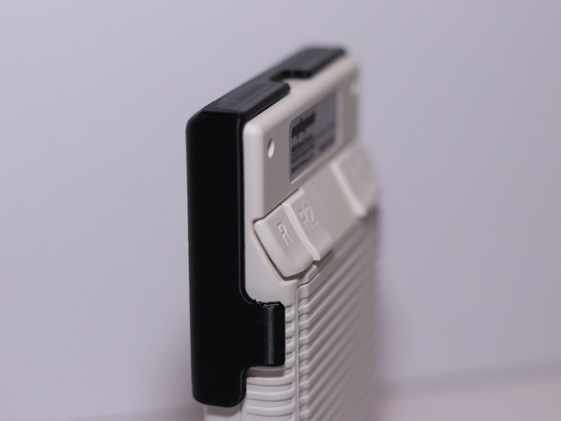 K&ouml;nnte beinhalten: Ein wei&szlig;es Handheld-Ger&auml;t mit einer schwarzen Schutzh&uuml;lle. Das Ger&auml;t hat einen kleinen Bildschirm und mehrere Kn&ouml;pfe. Der Text "Super NT" ist auf dem Ger&auml;t sichtbar.