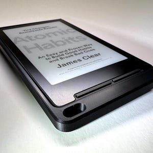 May include: A black e-reader displaying the title "Atomic Habits" by James Clear. The screen shows the text in white against a light background. The e-reader is in a black case.