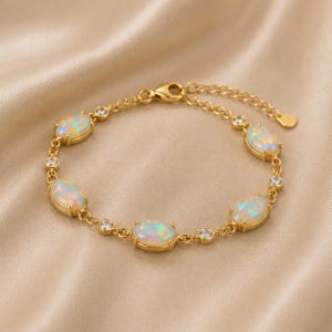 May include: A gold-toned chain bracelet featuring five oval-shaped iridescent opals set in metal bezels, alternating with small round clear crystals. The bracelet includes a delicate link chain, a lobster claw clasp, and an adjustable extender.