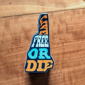 以下が含まれることがあります： ニューハンプシャー州の形をしたステッカーで、「Live Free or Die」という文字がレトロなフォントで書かれています。文字はオレンジ、ブルー、ホワイトです。