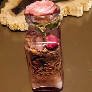 May include: A clear glass bottle with a pink wax seal on the top. The bottle is filled with dried herbs, flowers, and other botanicals.