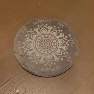 May include: A round gray slate coaster with a white mandala design and the words "Rephrase", "Yes", "Maybe", "No", and "Rephrase" around the edge.