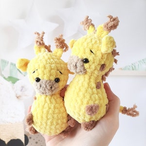 May include: Two crocheted stuffed giraffe toys, one larger than the other, are both yellow with brown accents. The smaller giraffe is sitting in front of the larger giraffe.