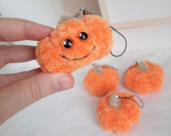 May include: Four orange plush pumpkin keychains. One pumpkin has a smiling face with black stitching and orange eyes.