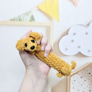 Puede incluir: Un juguete de dachshund de crochet en color amarillo mostaza. El juguete tiene ojos negros y una nariz negra.