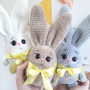 May include: Three crocheted bunny plushies with yellow ribbon bows. The bunnies are white, beige, and light blue.