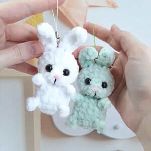 May include: Two crocheted bunny keychains, one white and one light green. Both bunnies have black eyes and pink noses.