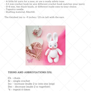 May include: White crocheted bunny amigurumi toy with pink ribbon, sitting on a pink surface with a pink wicker heart. The image includes text describing the materials and abbreviations used to make the toy.