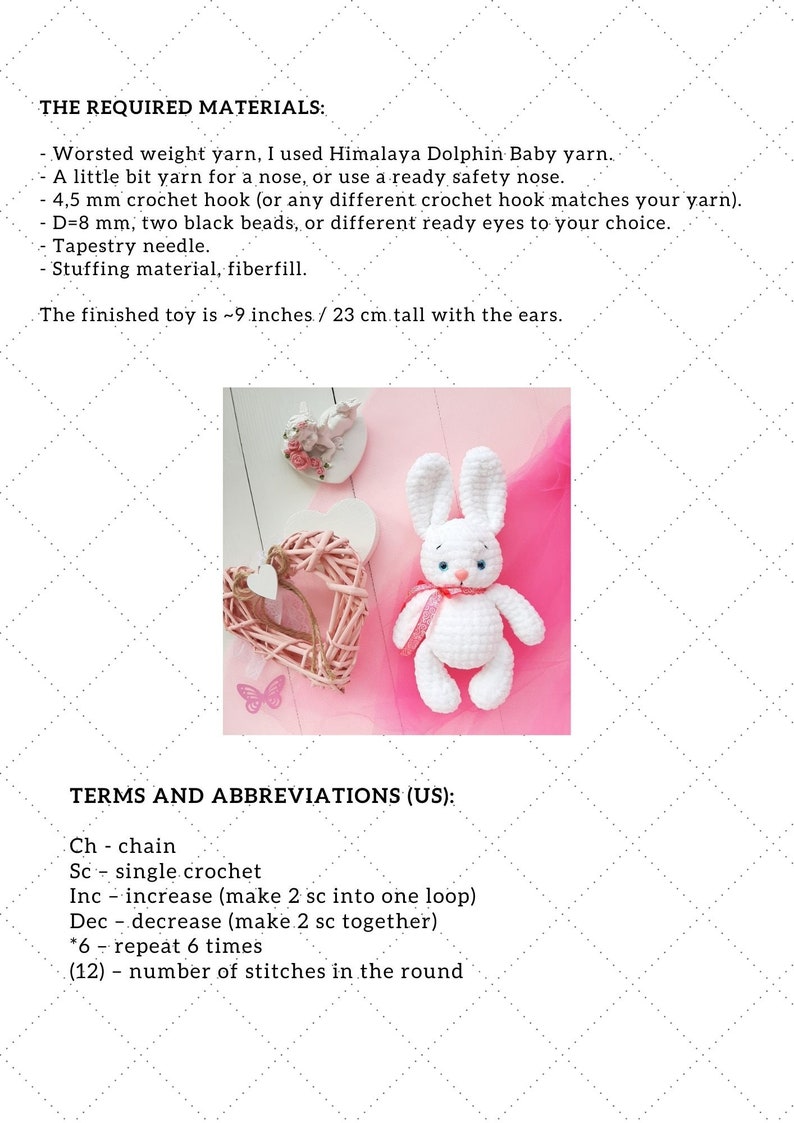 May include: White crocheted bunny amigurumi toy with pink ribbon, sitting on a pink surface with a pink wicker heart. The image includes text describing the materials and abbreviations used to make the toy.