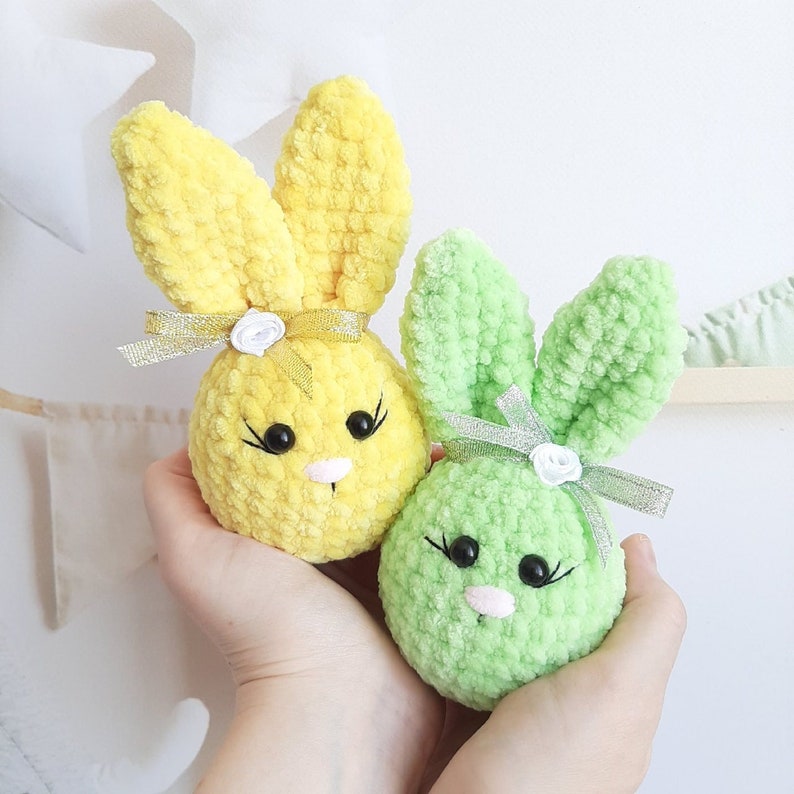 May include: Two crocheted bunny plushies, one yellow and one green, with white flower accents and silver ribbon bows.