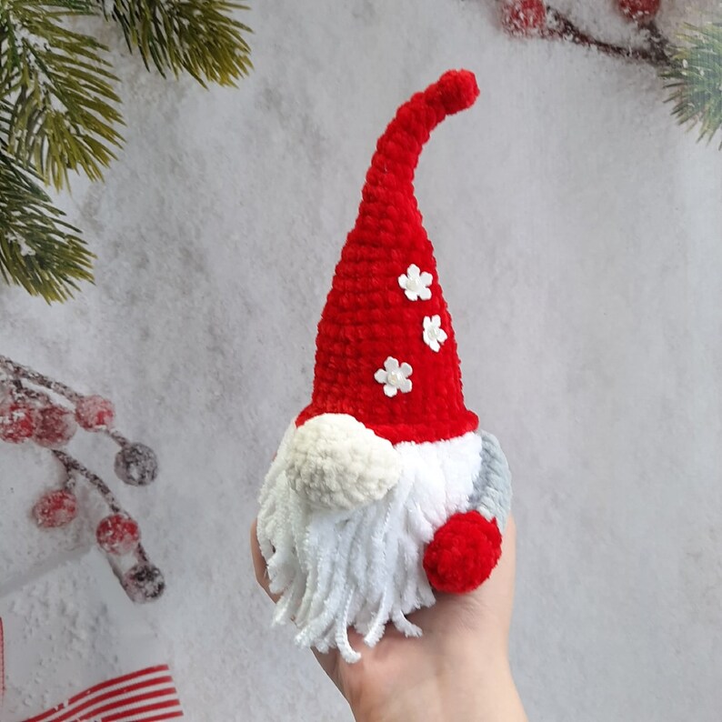 May include: A red crocheted gnome with a white beard and a red pom-pom on the hat. The hat has three white flowers on it.