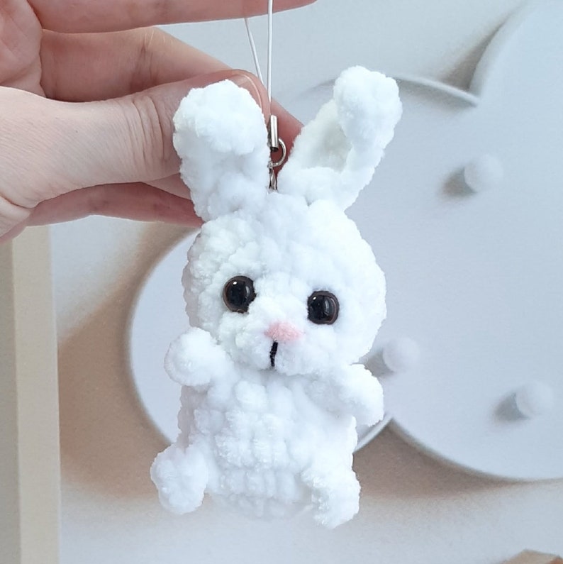 May include: A white crocheted bunny keychain with black eyes and a pink nose.
