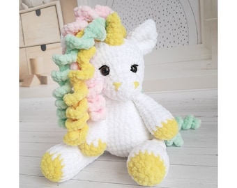 Puede incluir: Peluche de unicornio blanco de crochet con una melena y cola de hilo amarillo y rosa.