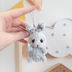May include: A gray crocheted bunny keychain with black eyes and a pink nose. The bunny is attached to a silver chain.