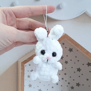 May include: White crocheted bunny keychain with black eyes and a pink nose. The bunny is attached to a white string.