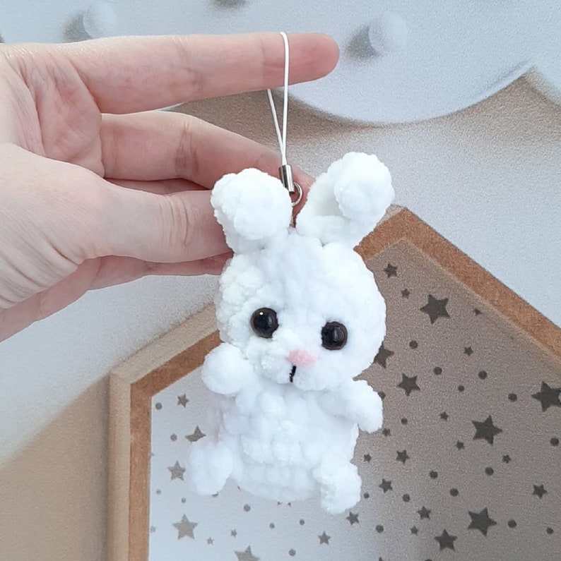 May include: White crocheted bunny keychain with black eyes and a pink nose. The bunny is attached to a white string.