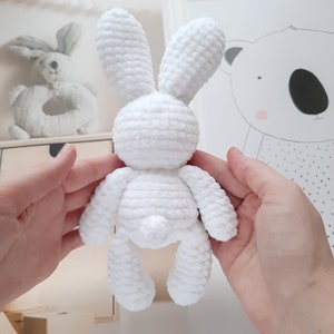 May include: A white crocheted bunny rabbit toy with long ears. The bunny is sitting in the palm of a person's hand.