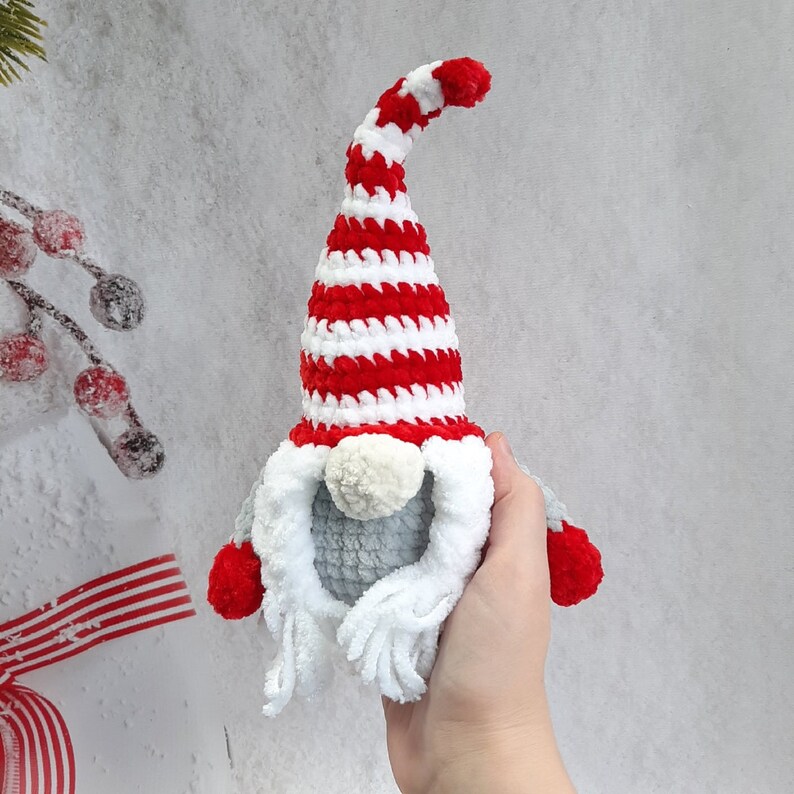 May include: A crocheted gnome ornament with a red and white striped hat and a gray beard. The gnome is holding a small red and white ball in its hand.