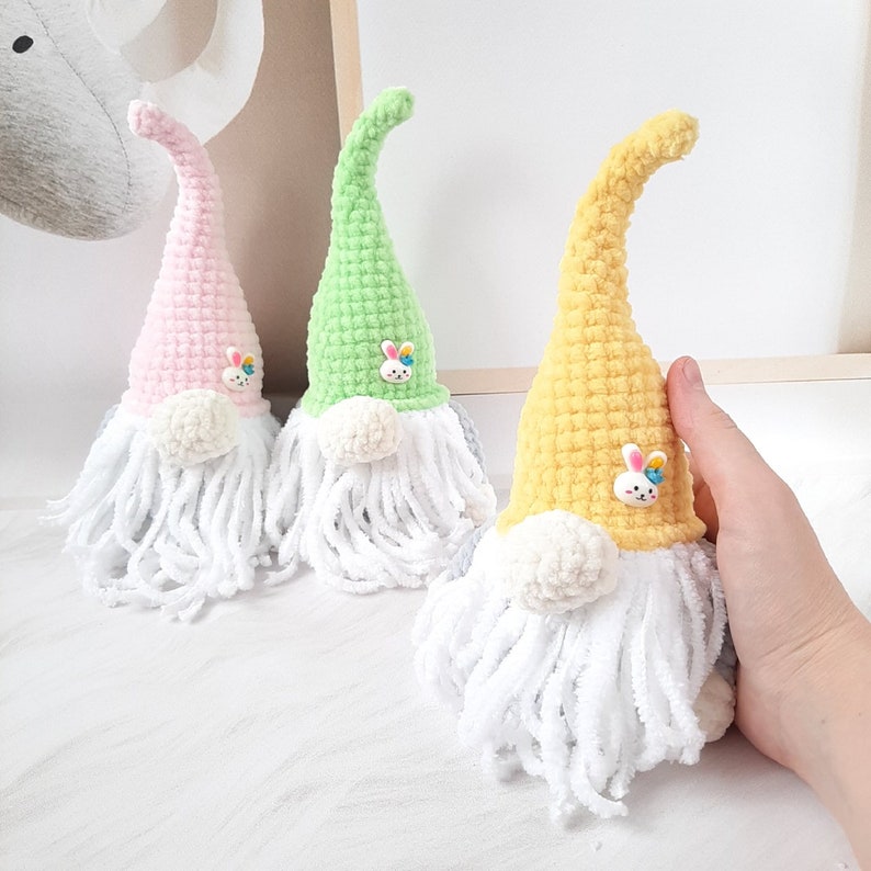 May include: Three crocheted gnomes with white beards and bunny buttons. The gnomes are pink, green, and yellow.
