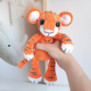 May include: A crocheted orange and white tiger plush toy with black stripes. The toy has a fluffy texture and large, round eyes.