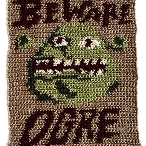 May include: Crocheted wall hanging with the text "Beware Ogre" in brown yarn. A green ogre face is in the center of the hanging.
