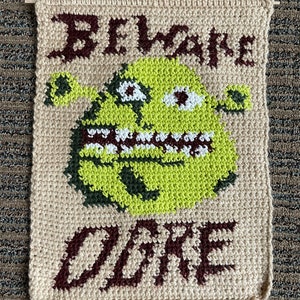 May include: Beige crocheted wall hanging with a green ogre face and the words "Beware Ogre" in brown yarn.