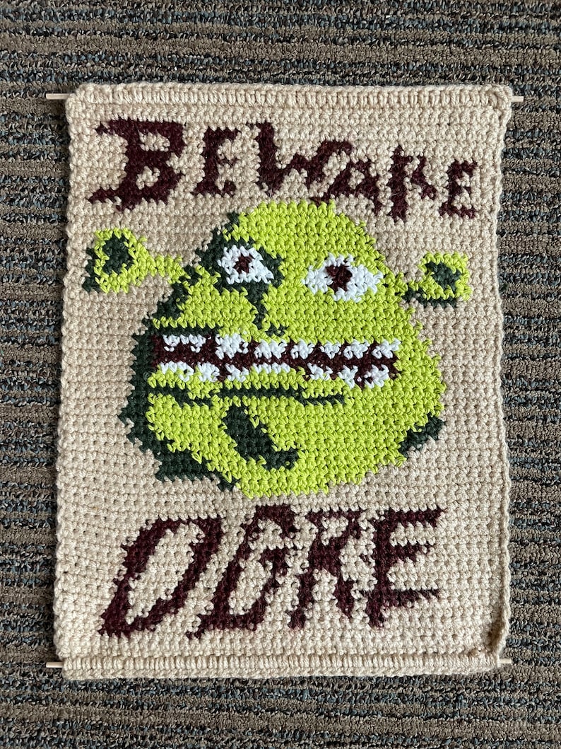 May include: Beige crocheted wall hanging with a green ogre face and the words "Beware Ogre" in brown yarn.