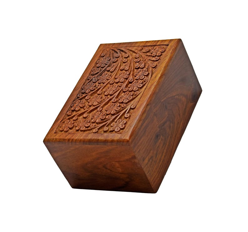 Puede incluir: Una caja de madera con un dise&ntilde;o floral tallado en la parte superior. La caja est&aacute; hecha de madera marr&oacute;n oscura y tiene una forma rectangular.