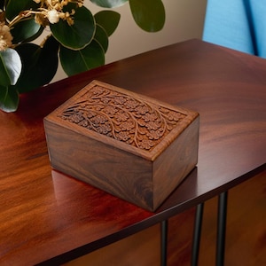 Puede incluir: Una caja de madera con un dise&ntilde;o floral tallado. La caja est&aacute; hecha de madera oscura y tiene una forma rectangular.